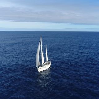 Segelboot mit wei&szlig;en Segeln auf ruhiger blauer See unter einem teilweise bew&ouml;lkten Himmel.