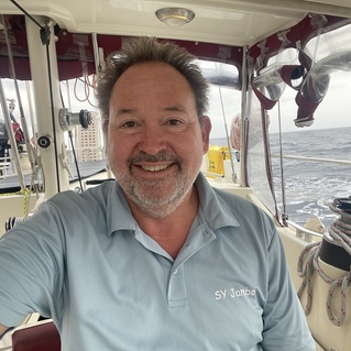 L&auml;chelnder Mann in einem Segelboot, umgeben von maritimer Ausr&uuml;stung und offener See.