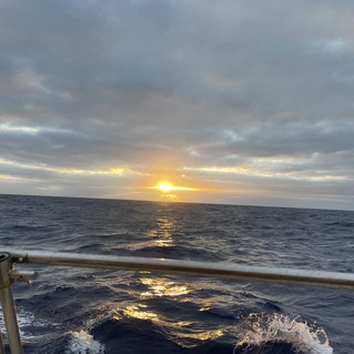 Sonnenuntergang &uuml;ber dem Meer mit reflektierenden Wellen, sichtbar von einem Boot mit reling.