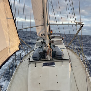 Blick von der Yacht auf das Deck mit Segeln und Wasser im Hintergrund bei Sonnenuntergang.