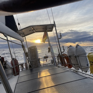 Sicht auf das Deck eines Segelbootes mit Sonnenuntergang &uuml;ber dem Meer im Hintergrund.