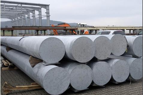 Lagerfl&auml;che mit mehreren gro&szlig;en, zylindrischen Stahlrohren auf Holzpaletten, im Hintergrund leichte Industriearchitektur.