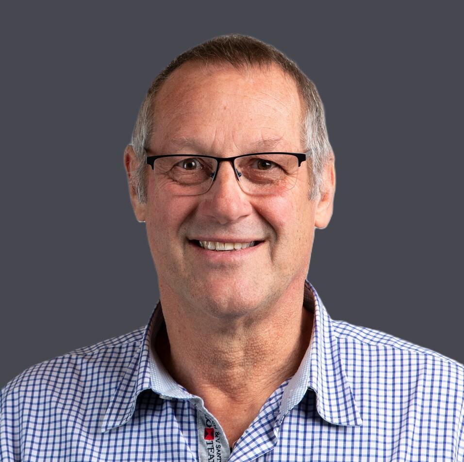 L&auml;chelnder Mann mit Brille und kariertem Hemd vor einer wei&szlig;en, neutralen Hintergrundfl&auml;che.