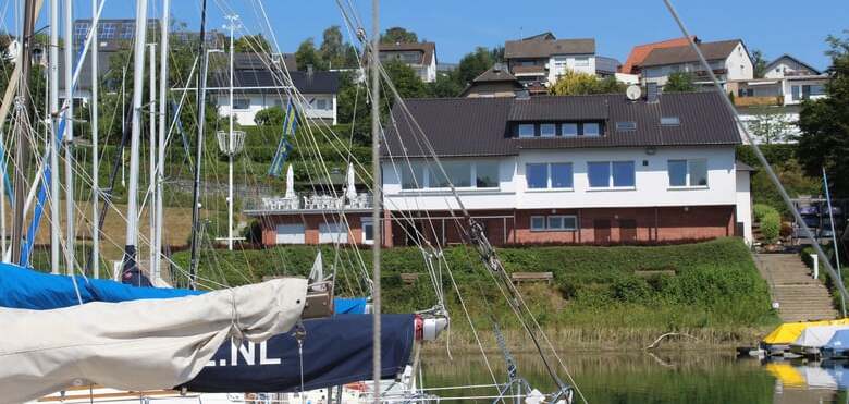 Yachten im Hafen mit einem modernen Geb&auml;ude und Wohnh&auml;usern im Hintergrund unter klarem blauen Himmel.