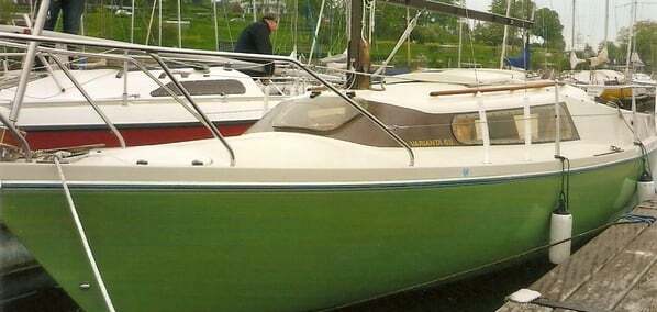 Segelboot mit gr&uuml;ner Rumpffarbe am Hafen, zwei Personen sind in der N&auml;he mit anderen Yachten im Hintergrund.