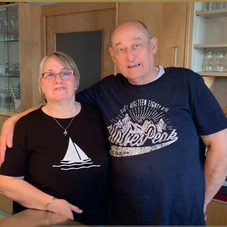 Paar in einer K&uuml;che, stehen nahe beieinander, l&auml;cheln in die Kamera, tragen l&auml;ssige Freizeitkleidung.