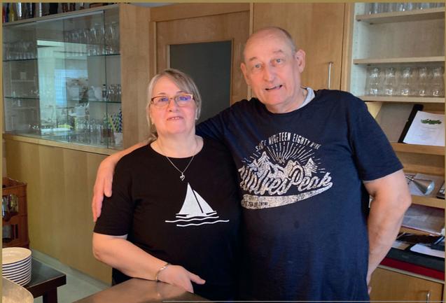 Paar in einer K&uuml;che, stehen nahe beieinander, l&auml;cheln in die Kamera, tragen l&auml;ssige Freizeitkleidung.