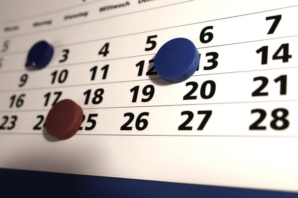 Nahaufnahme eines Kalenders mit blauen und roten Markierungen auf den Tagen 12, 19 und 26.