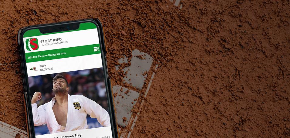 Smartphone auf einem mit Tennisplatz-Kreide markierten Sandplatz, zeigt Sportnachricht zu Johannes Frey.