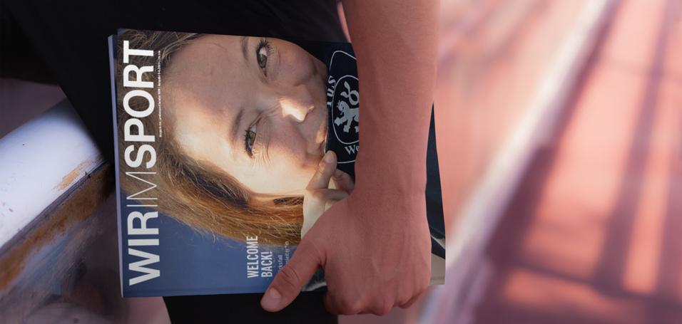 Nahaufnahme einer Person, die ein Magazin mit der Aufschrift &bdquo;WIR | SPORT&ldquo; h&auml;lt, w&auml;hrend sie auf einer Bank sitzt.